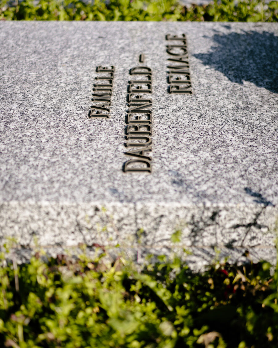 Lettres en bronze sur un monument en pierre, dans la verdure d’un cimetière